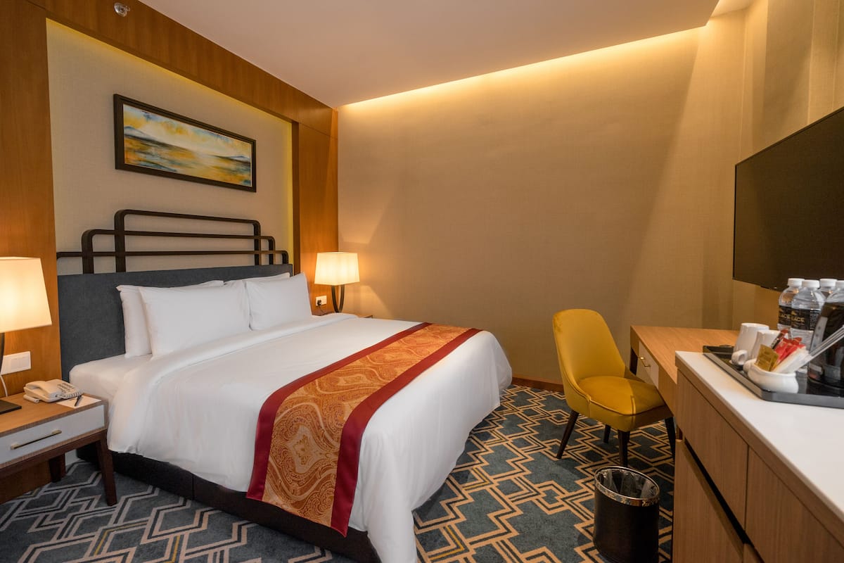A hotel room with a bed, bedside lamps, a desk with a chair, a trash can, and a television.