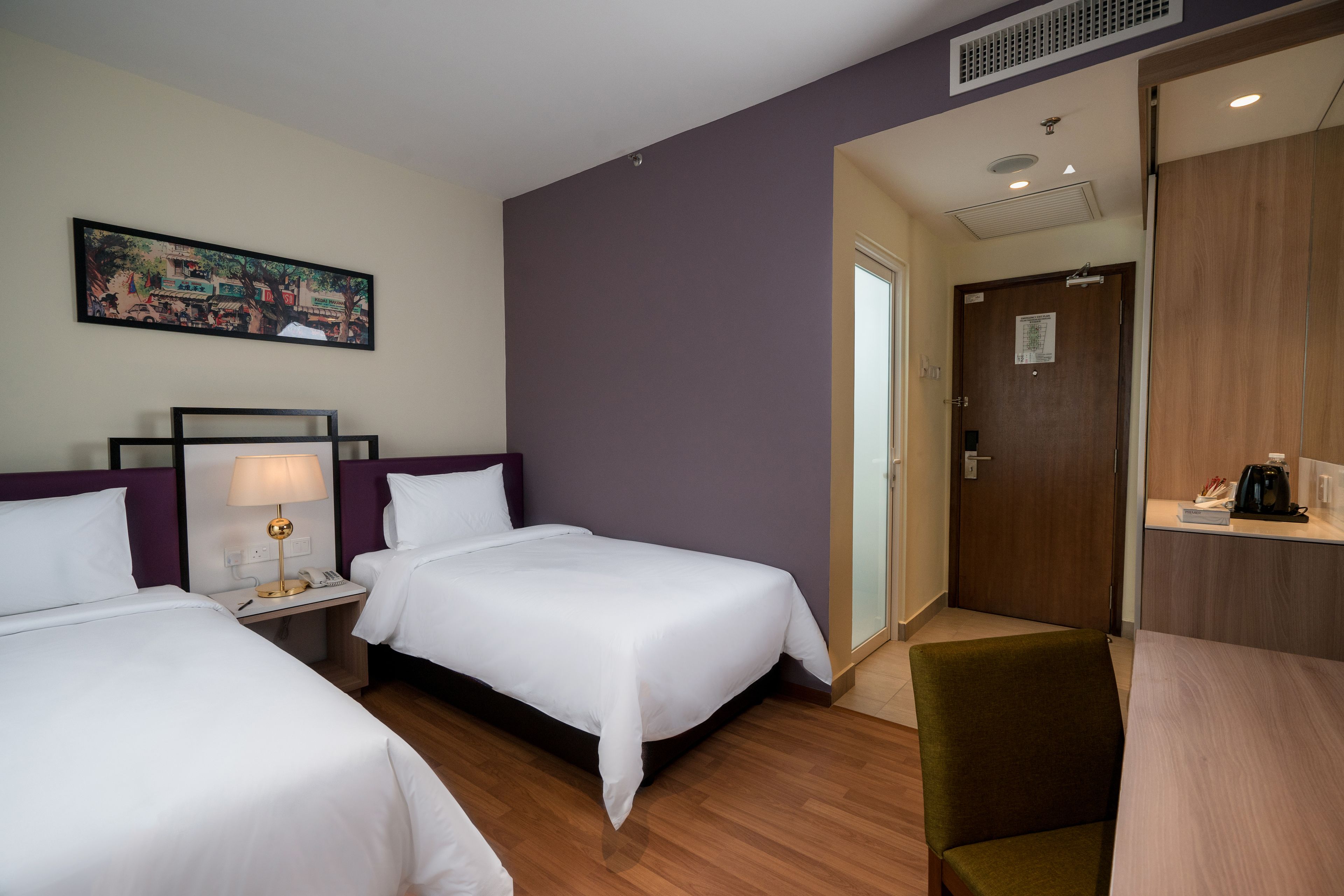 A hotel room with two beds, a desk, a chair, a painting on the wall, and a door leading to the bathroom.