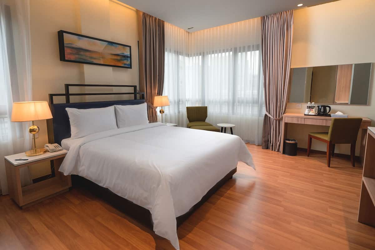 A hotel room with a large bed, bedside tables with lamps, a desk with a chair, and a large window with curtains.