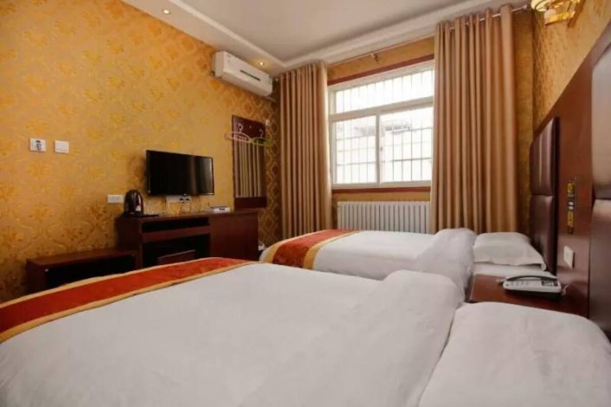 Quarto de hotel com duas camas, televisão, escrivaninha e janela com cortinas.