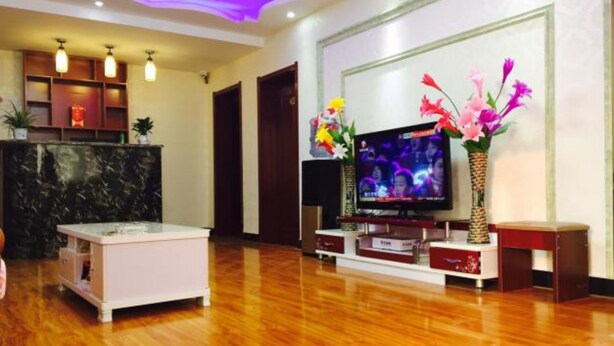 A living room with a flat-screen TV, wooden flooring, a white coffee table, and a decorative vase with flowers.