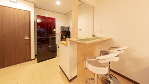 Une cuisine compacte équipée d’un four à micro-ondes, d’un réfrigérateur et d’un petit îlot central avec un évier et une chaise.