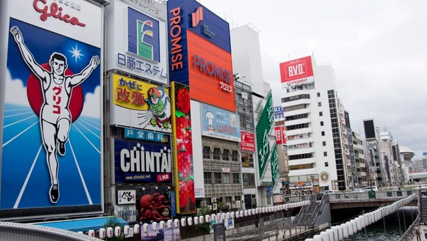 Une vue urbaine avec un grand panneau publicitaire bien visible, sur lequel on aperçoit une silhouette en mouvement et le mot « Glico ».