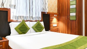 A hotel room with a bed, two green pillows, a wooden headboard, a nightstand with a phone, and a wall-mounted information board. - Itsy Hotels Elmas Golden Key (Bengaluru)