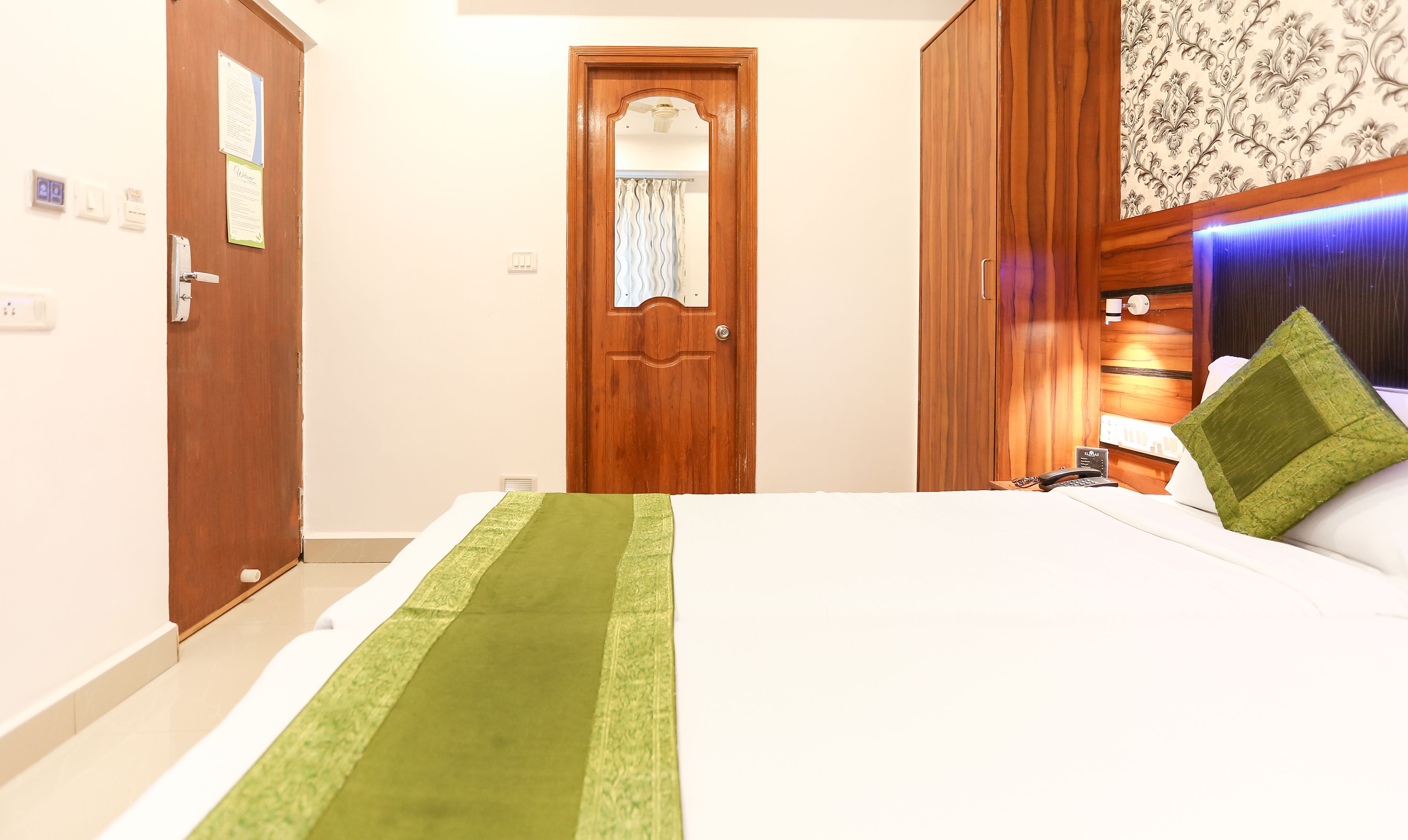 Habitació d'hotel amb un llit, un armari de fusta, una porta de bany i una tauleta de nit amb una làmpada i un telèfon.