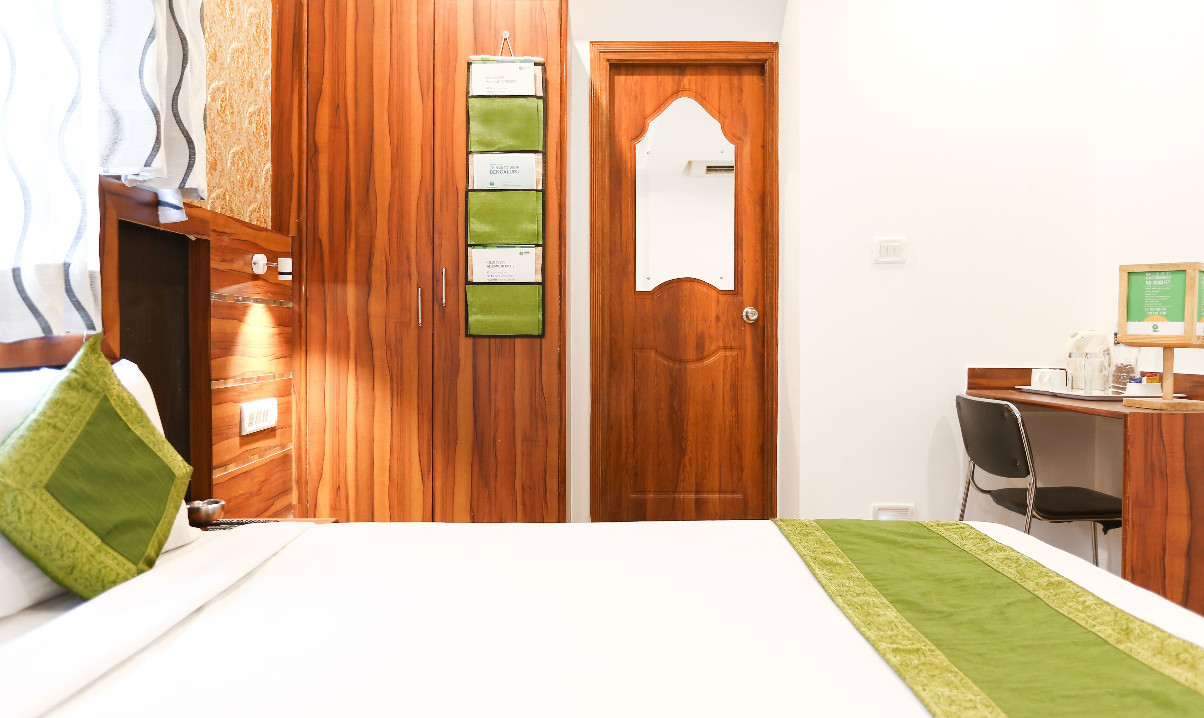 A hotel room with a wooden wardrobe, a desk with a chair, and a bed with a green bedspread.