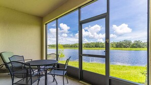 Une terrasse couverte, dotée d’une table et de chaises, qui offre une vue sur un lac bordé de rives verdoyantes et d’arbres.