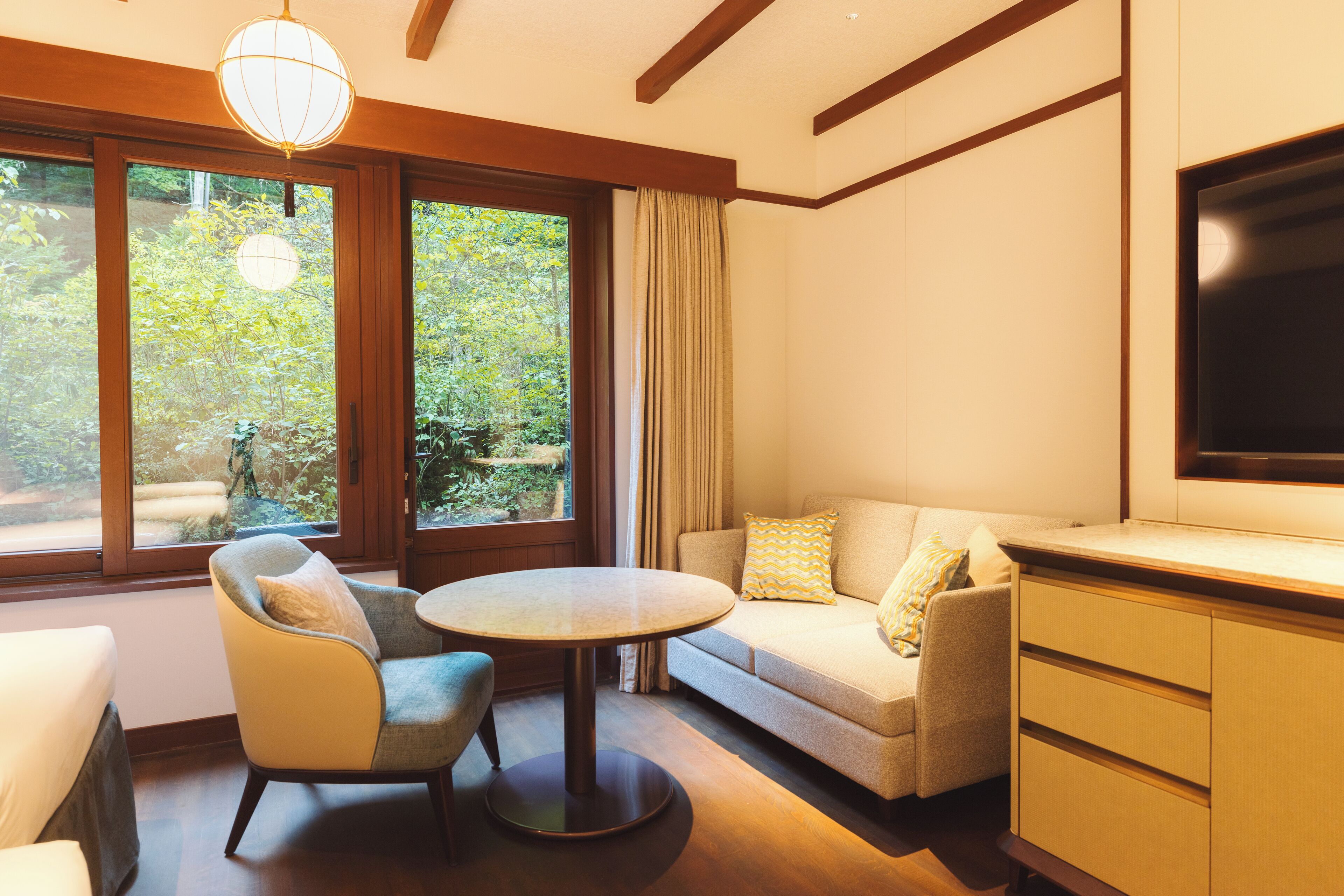 A modern living room with a sofa, armchair, round table, and a TV on a wooden cabinet.