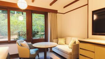 A modern living room with a sofa, armchair, round table, and a TV on a wooden cabinet.