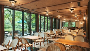 Un restaurante con mobiliario de mimbre, ventanas amplias e iluminación en el techo.
