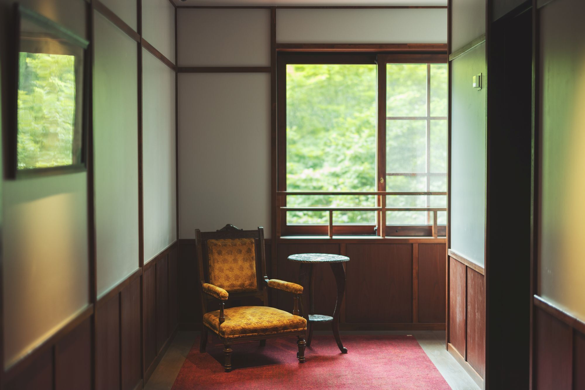 Une pièce avec une chaise en bois, une petite table ronde et une fenêtre donnant sur un paysage verdoyant.