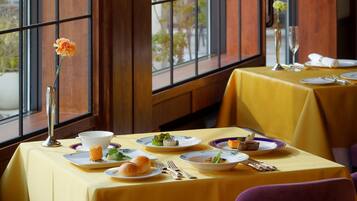 A restaurant with tables set for dining, a vase with flowers, and a view through large windows.