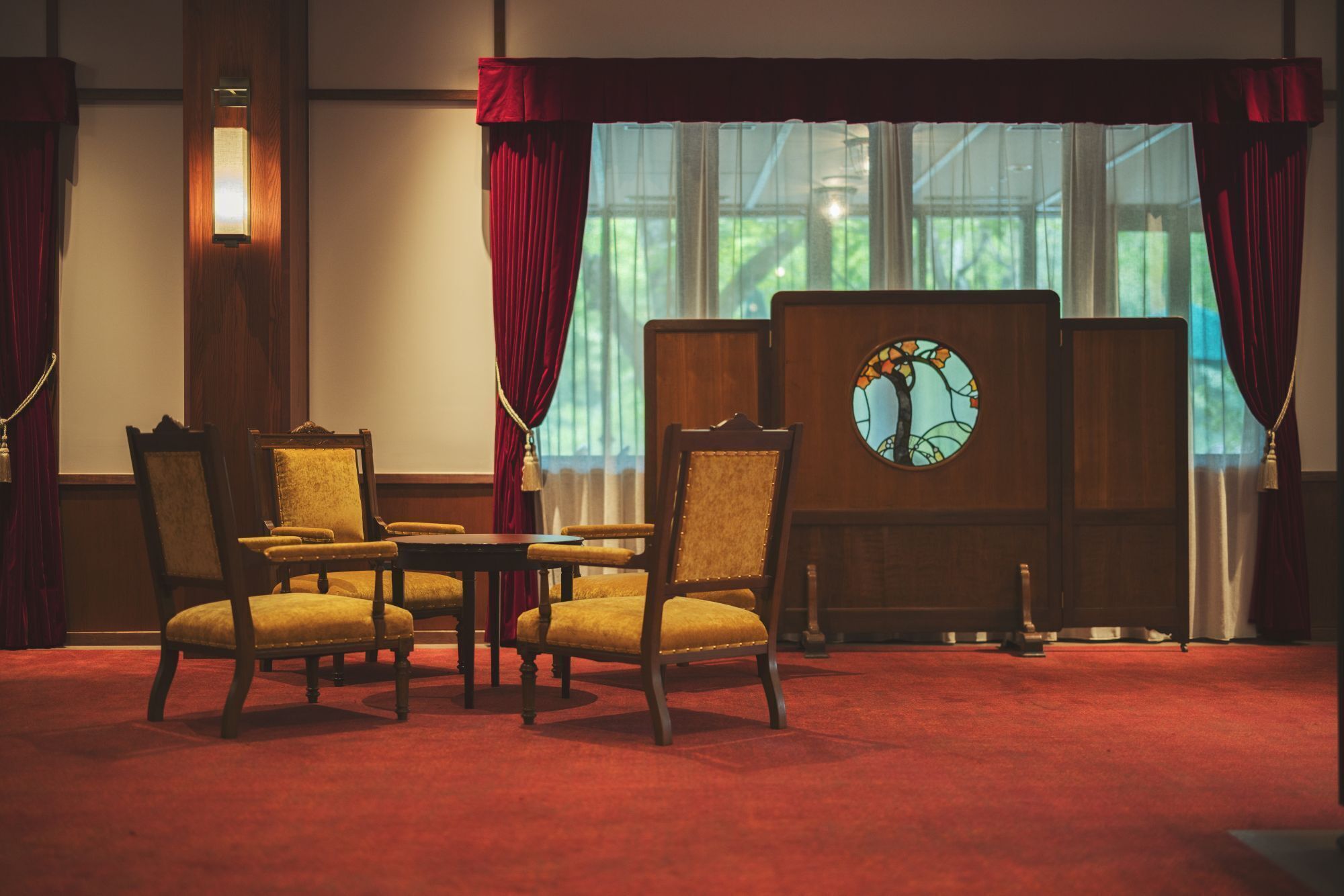 A room with a red carpet, wooden furniture, and a large window with curtains.