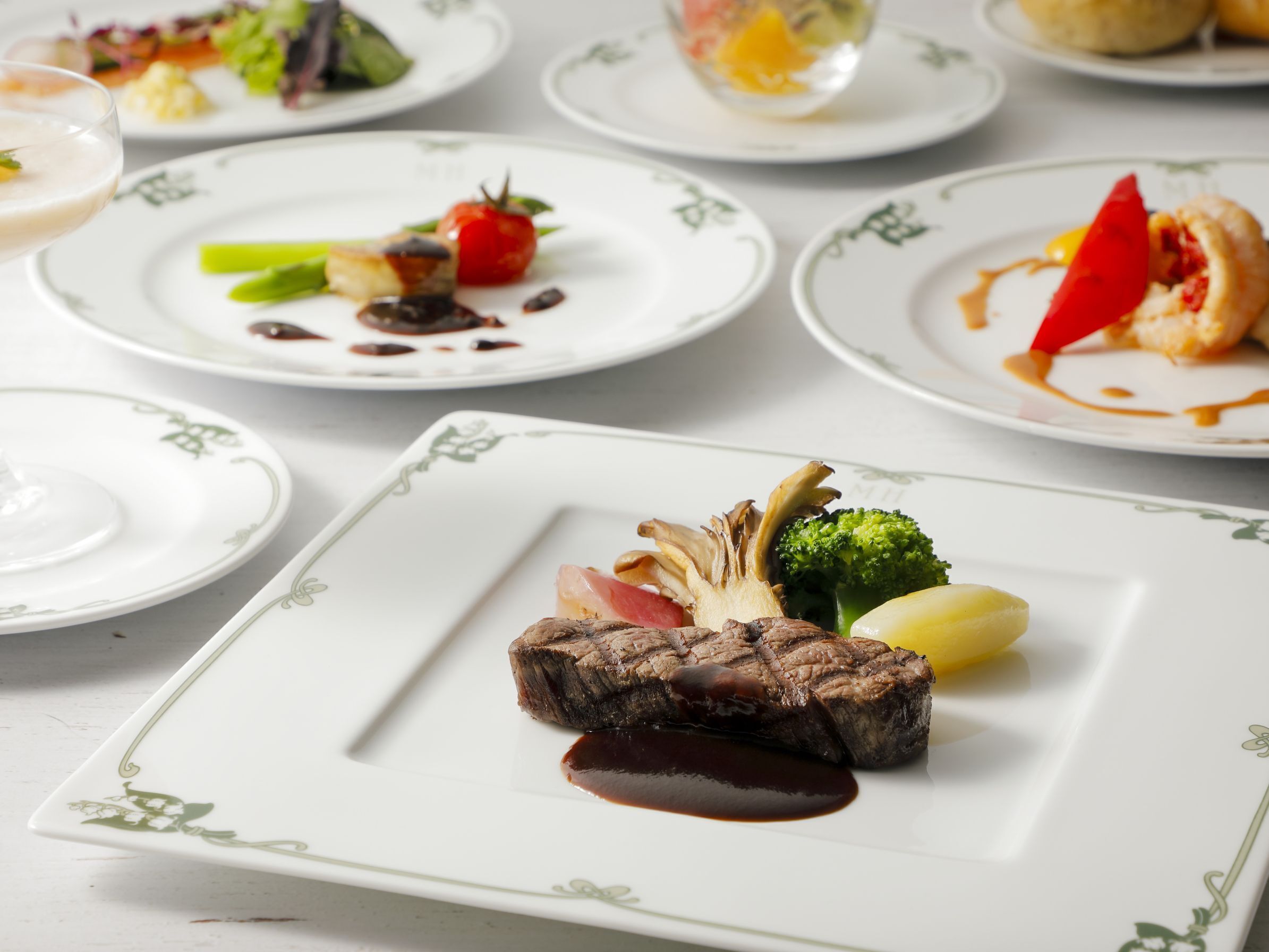 A dining table with various plates of food, including a steak with sauce, vegetables, and a dessert.