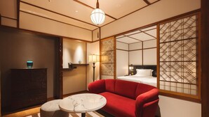 Habitación de hotel con sofá, una mesita redonda pequeña, lámpara, florero decorativo y cama con cabecero.