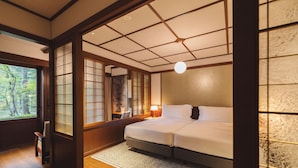 Un dormitorio tradicional japonés con suelo de tatami, una cama grande, puertas correderas y vistas al exterior.