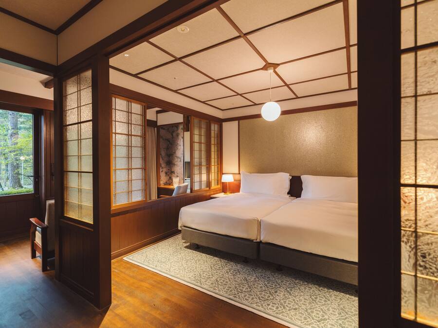 A traditional Japanese-style bedroom with tatami flooring, a large bed, sliding doors, and a view of the outdoors.