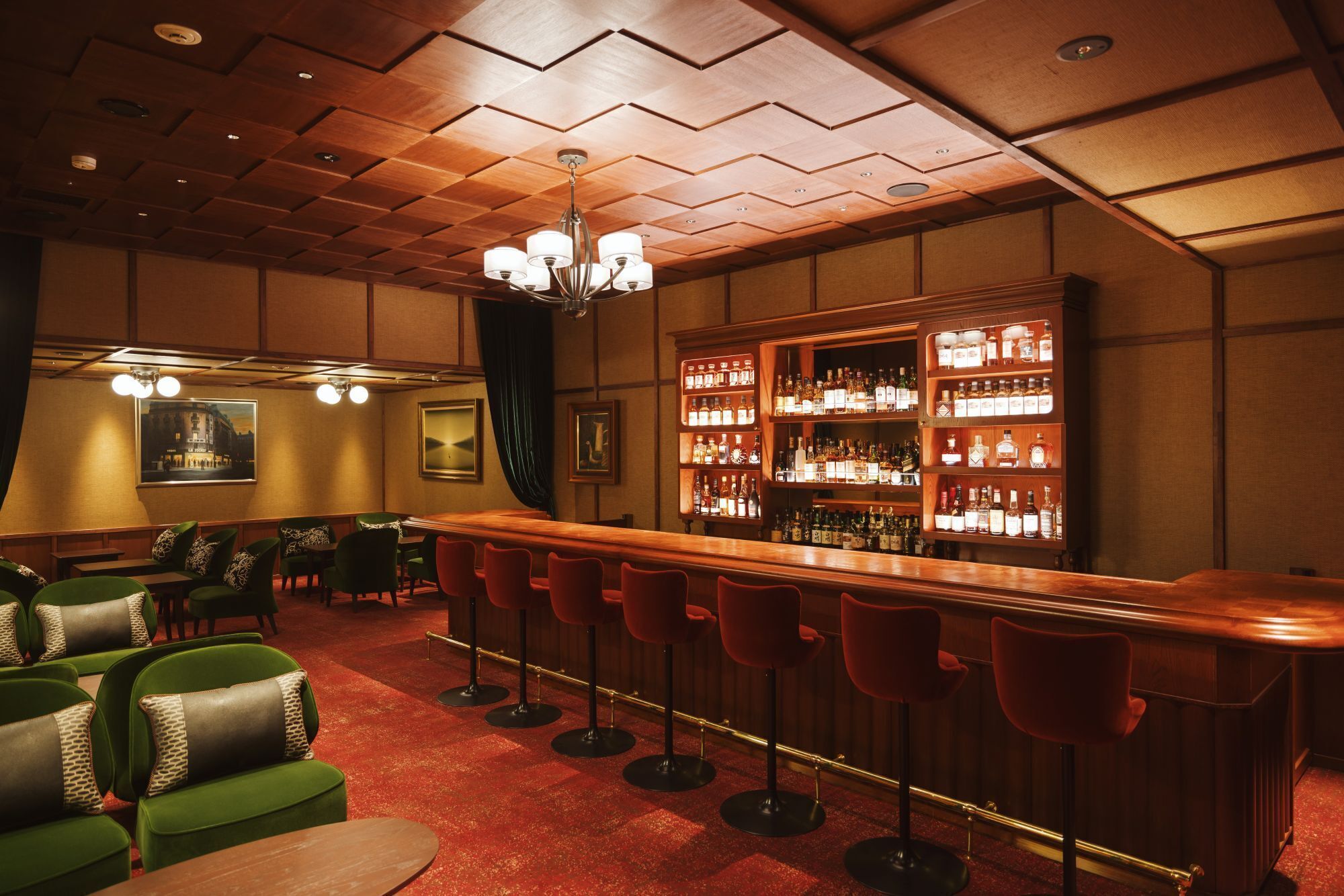 Zona de bar con techo de paneles de madera, taburetes tapizados en verde y barra con estantes llenos de botellas de licor.