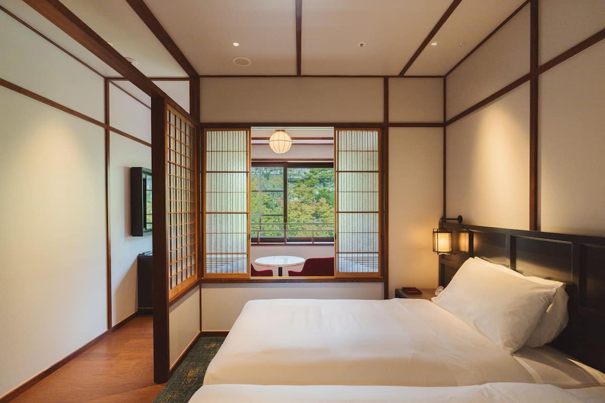 A traditional Japanese-style room with tatami flooring, a low wooden bed, sliding shoji doors, and a view of greenery outside.