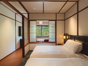 A traditional Japanese-style room with tatami flooring, a low wooden bed, sliding shoji doors, and a view of greenery outside.