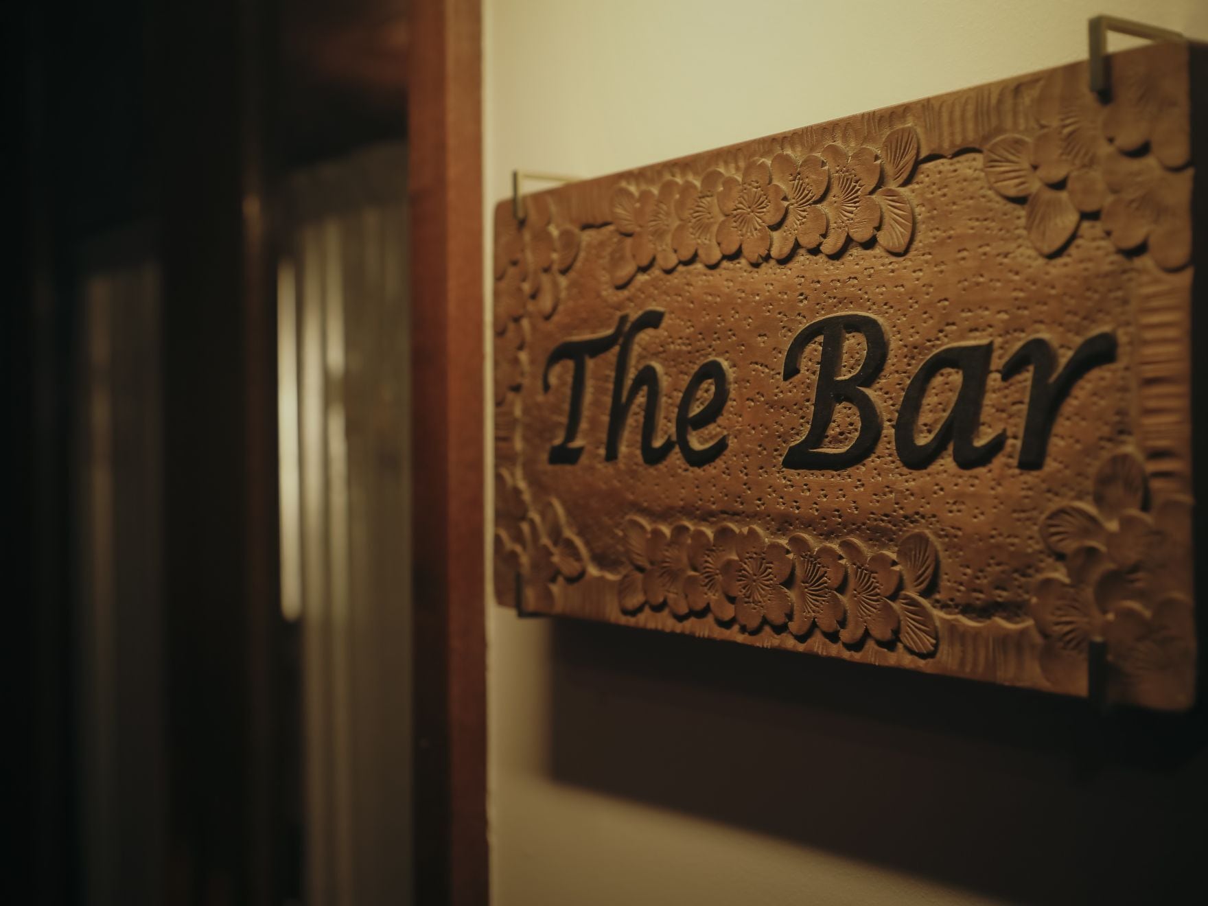 Uma placa de madeira com a inscrição 'The Bar' gravada, fixada em uma parede.