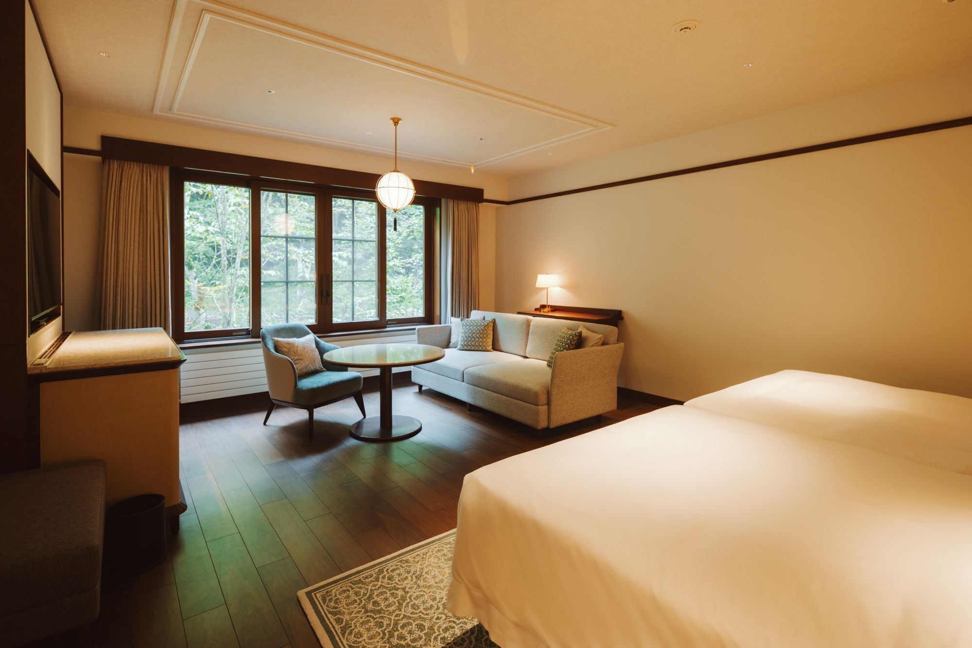 A hotel room with a bed, a sofa, a chair, a small table, and a window with curtains.