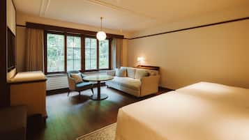 A hotel room with a bed, a sofa, a chair, a small table, and a window with curtains.