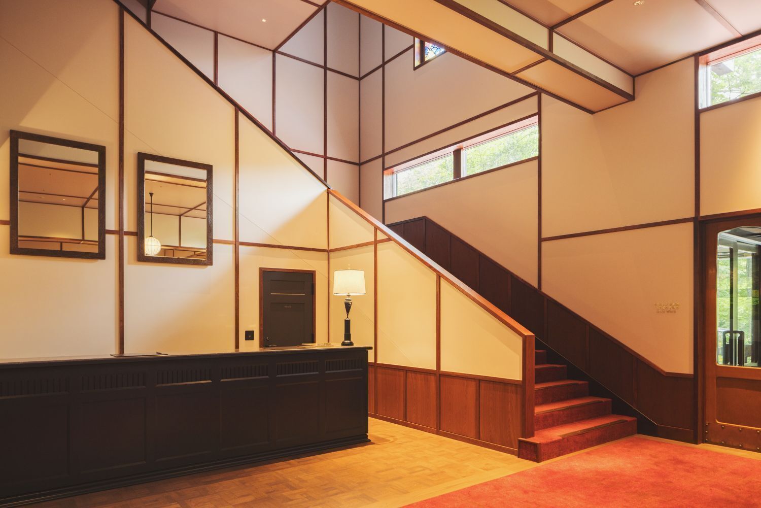 A hotel lobby with a reception desk, a staircase, and large windows.