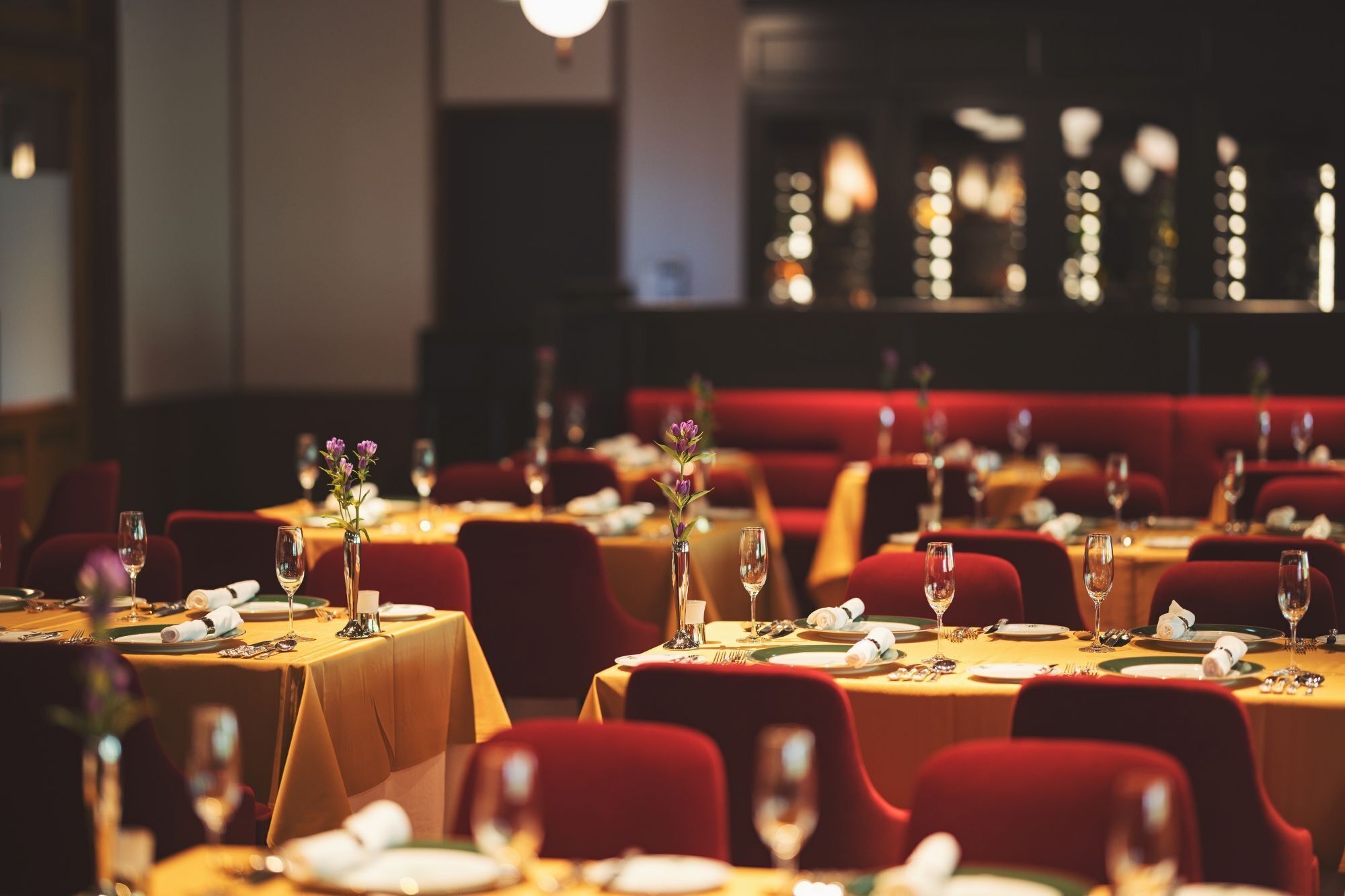 A restaurant with tables set for dining, red upholstered chairs, and a warm ambient lighting.