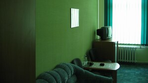 A room with a green wall, a small table with a television, a couch, and a radiator. - Hotel  Flat 5678 (Odesa)