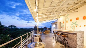 A balcony with a glass table and chairs, a bar area with stools, and a view of the surrounding landscape. - Ohana Pererenan (Pererenan)