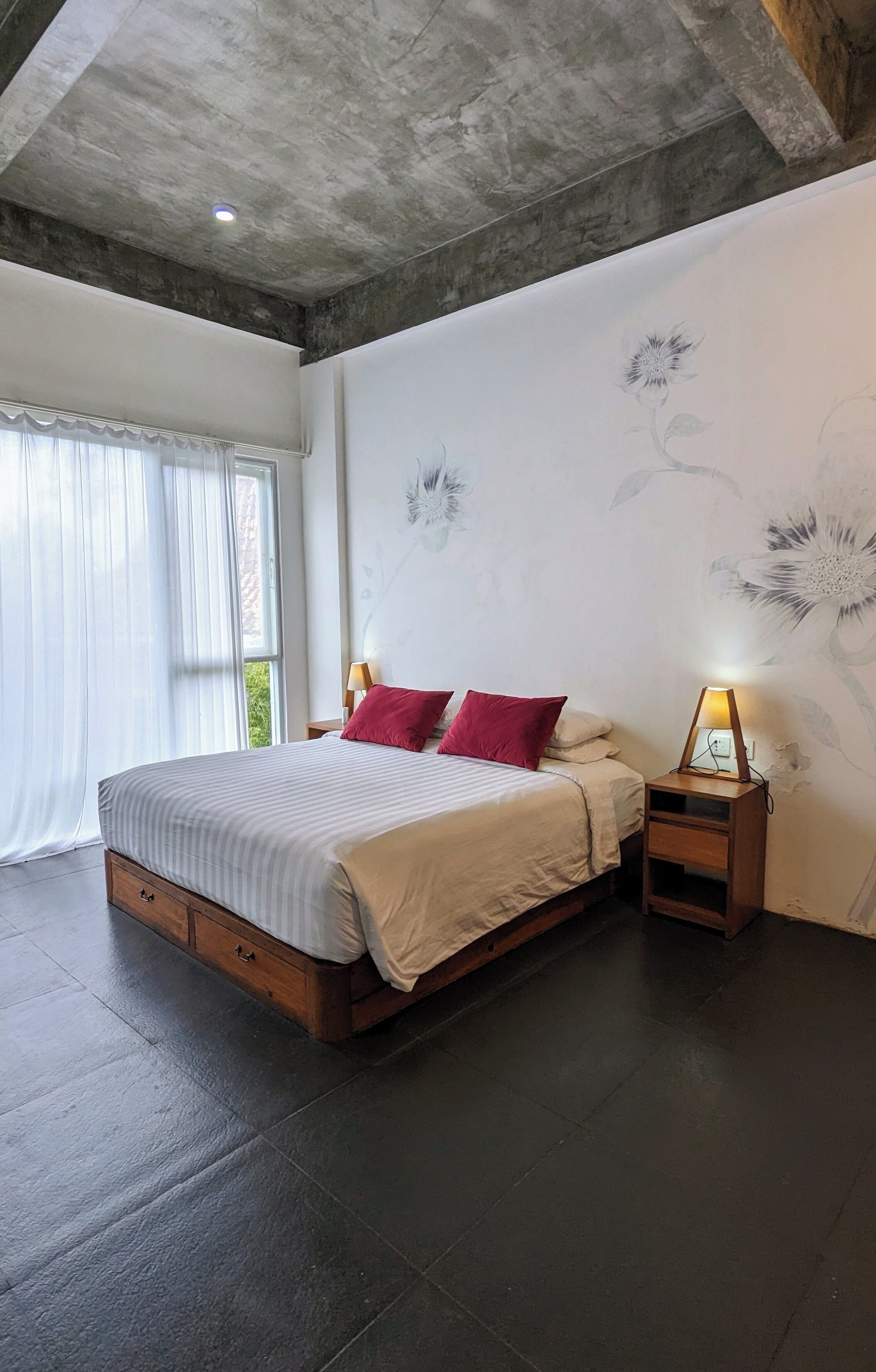 A bedroom with a large bed, a nightstand, a lamp, and a window with curtains.
