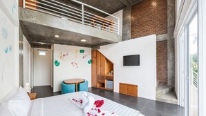 A hotel room with a large bed, a wooden desk, a TV, and a balcony with a brick wall. - Ohana Pererenan (Pererenan)