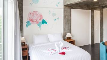 A modern bedroom with a large bed, a ceiling fan, a wooden nightstand, a blue chair, and a balcony with a railing.
