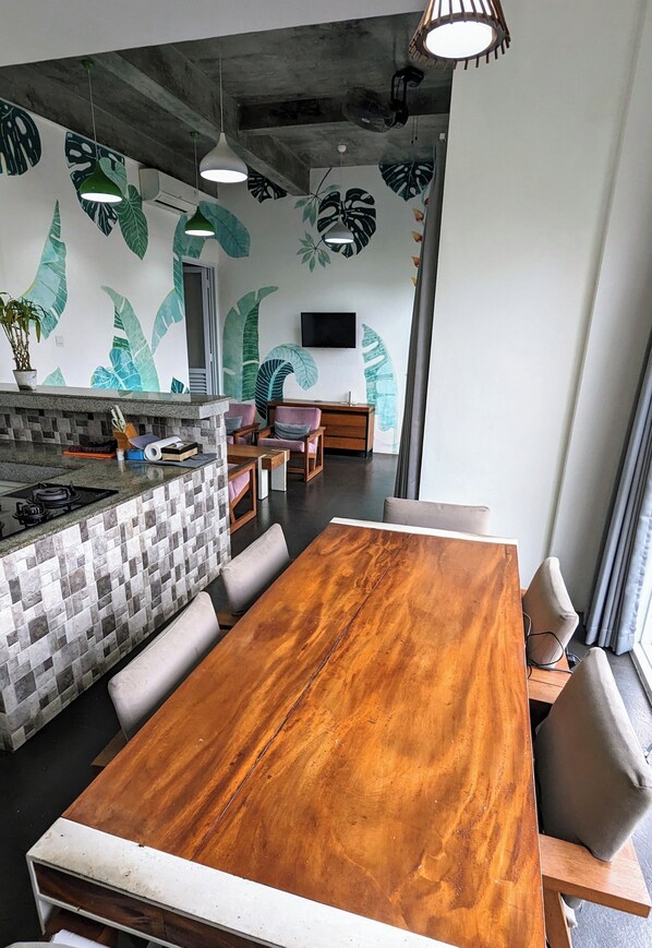 A modern kitchen with a tiled backsplash, a wooden dining table, and a seating area with chairs. - Ohana Pererenan (Pererenan)