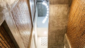 A staircase with a white handrail, brick walls, and a modern light fixture at the top. - Ohana Pererenan (Pererenan)
