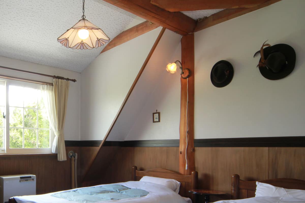 A room with two wooden beds, a window with curtains, a radiator, and a hanging light fixture.