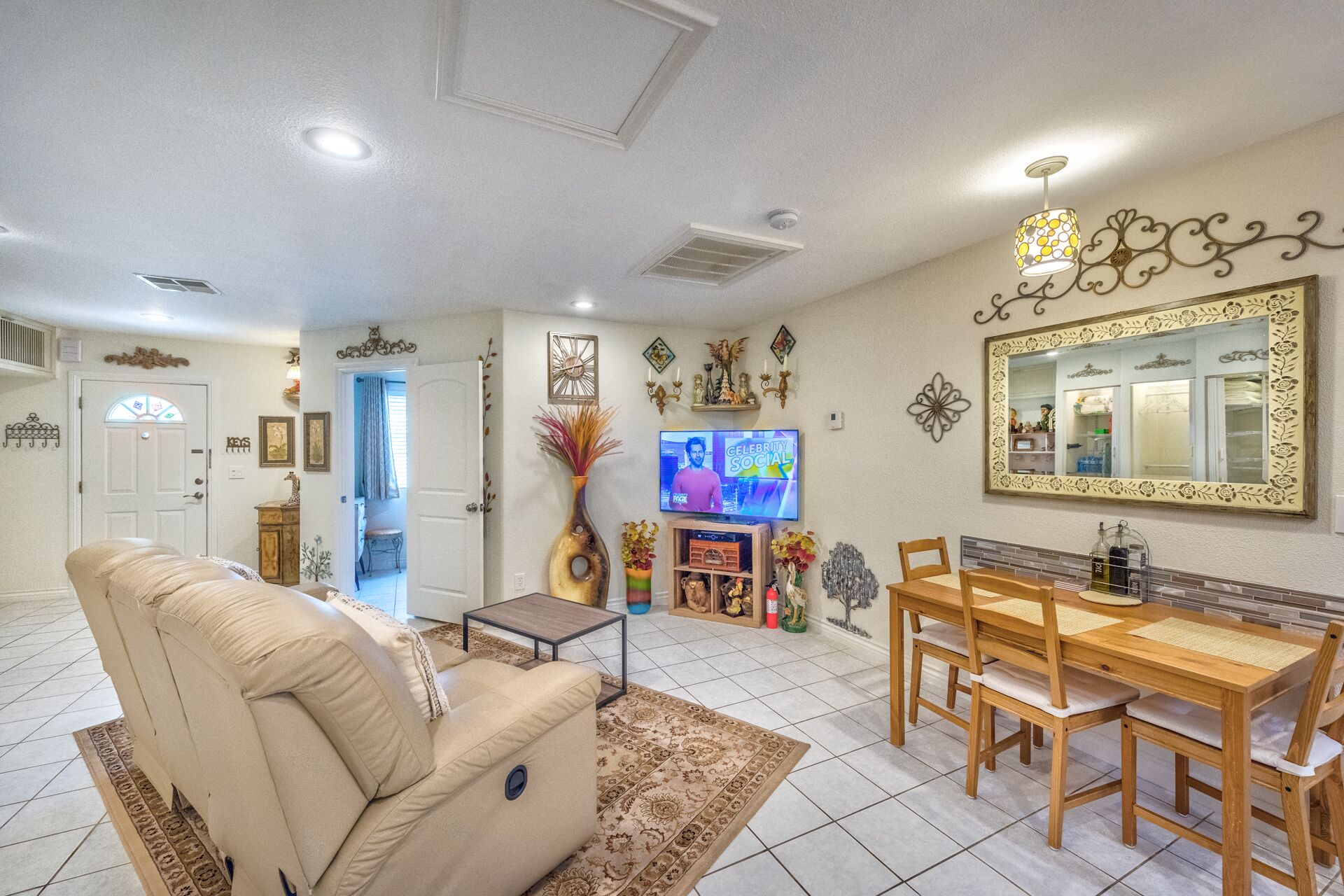 A living room with a beige sofa, a wooden dining table with chairs, a television, and decorative wall art.