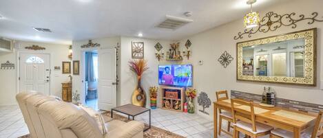 A living room with a beige sofa, a wooden dining table with chairs, a television, and decorative wall art.