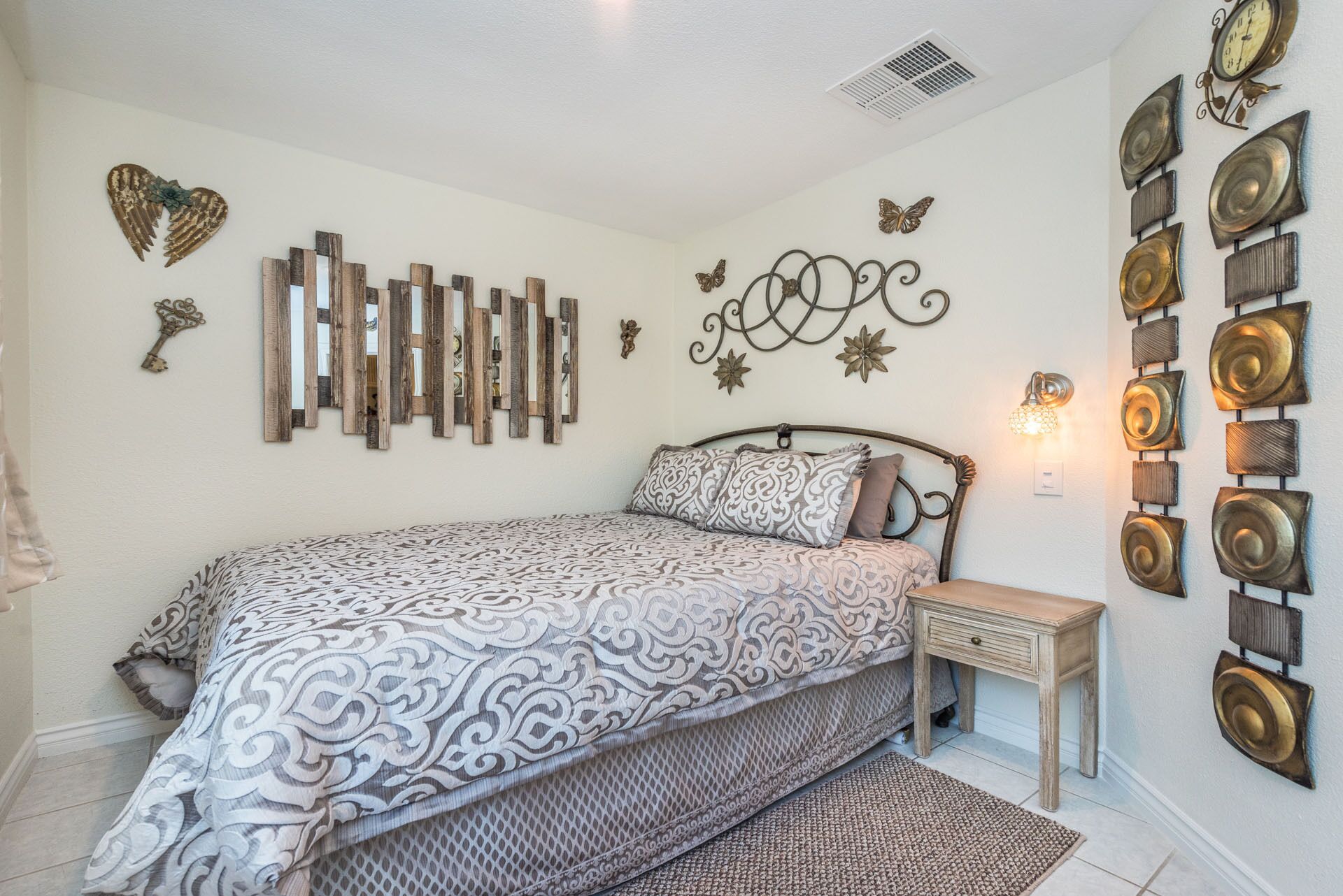 A bedroom with a bed, a nightstand, decorative wall art, and a wall-mounted light fixture.