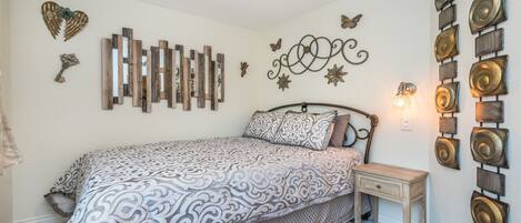 A bedroom with a bed, a nightstand, decorative wall art, and a wall-mounted light fixture.