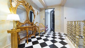 Un pasillo lujoso con suelo a cuadros, muebles dorados ornamentados y un espejo con marco dorado.