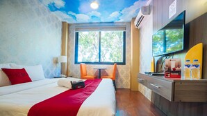 Habitación de hotel con cama, escritorio, silla, televisor y ventana con vista a árboles.