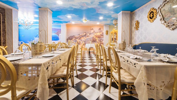 Un comedor con piso a cuadros, sillas doradas y mesas dispuestas para una comida.