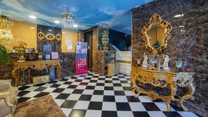 Un lobby lujoso con piso a cuadros, muebles dorados ornamentados, una araña y una pared de mármol con un espejo grande.