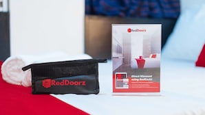 Une présentation promotionnelle de RedDoorz comprenant une offre de réduction immédiate, un sac noir et une serviette blanche roulée, le tout placé sur un lit.