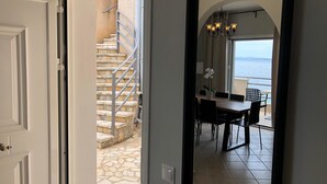 A view through an open door into a dining area with a stone staircase, a table with chairs, and a view of the sea through an arched window. - Glyfa Beach Villas (Corfu)