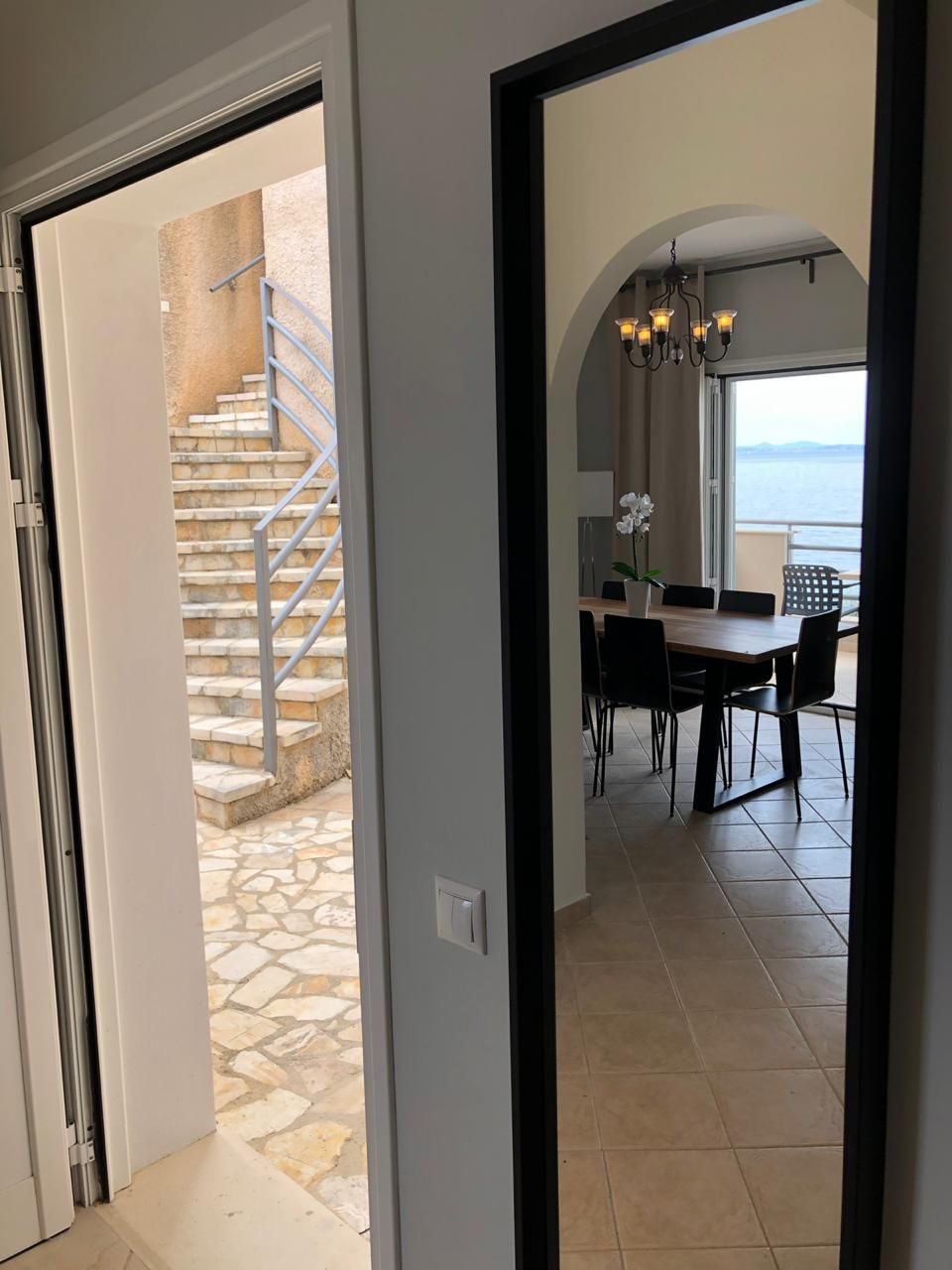 A view through a doorway to a dining area with a table, chairs, and a chandelier. A staircase with a metal railing is visible in the background.