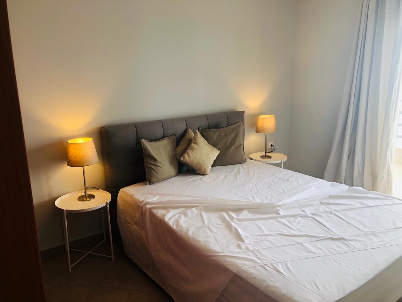 A neatly made bed with white bedding, two bedside lamps, and a headboard.