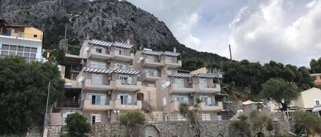 Um edifício residencial com várias andares e varandas, com montanhas ao fundo.